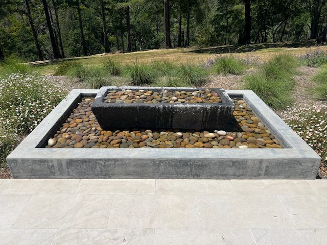 Modern outdoor stone water feature with a central basin and surrounding rock bed.