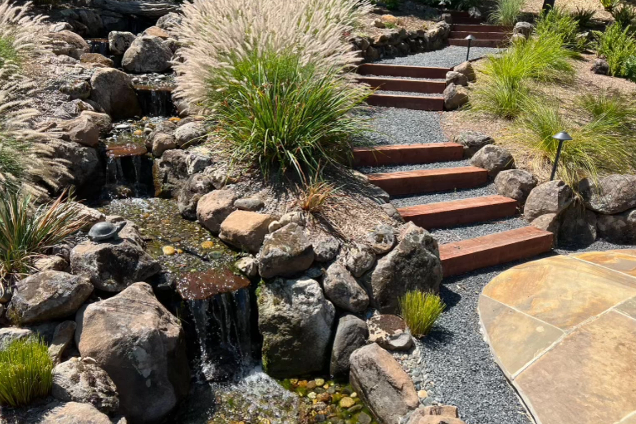 Stone steps beside a small waterfall and lush greenery.