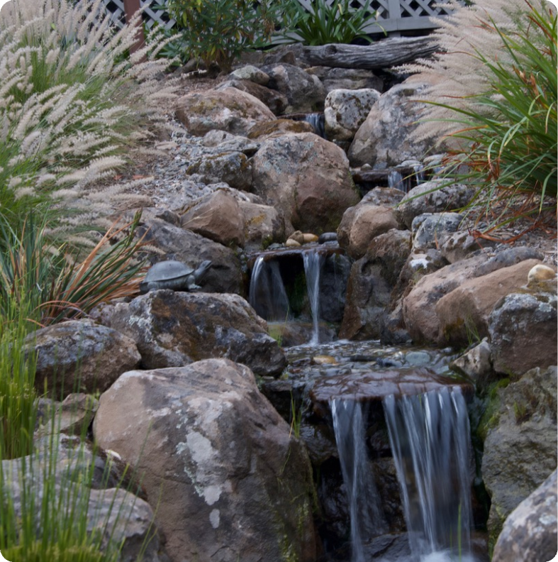 A small waterfall flowing over rocks in a garden setting.