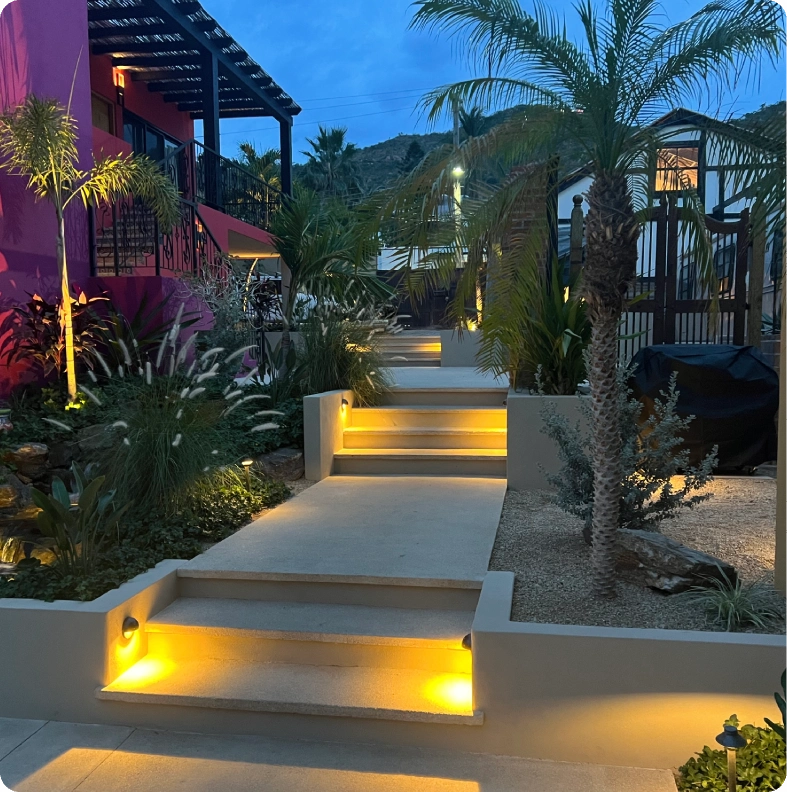 Illuminated outdoor steps with warm lighting and tropical plants at dusk.