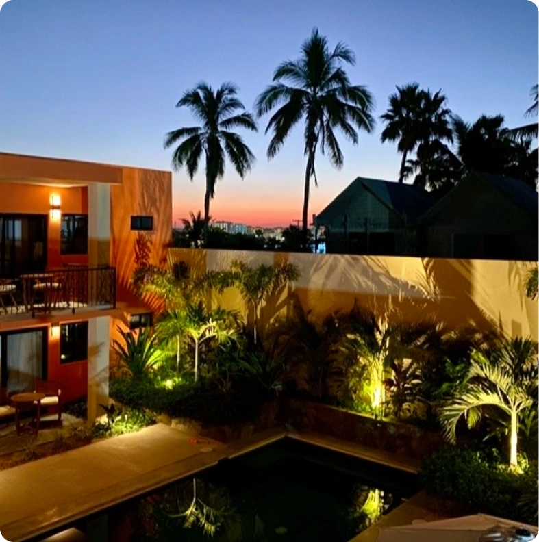 Modern tropical house with palm trees at sunset and illuminated pool.