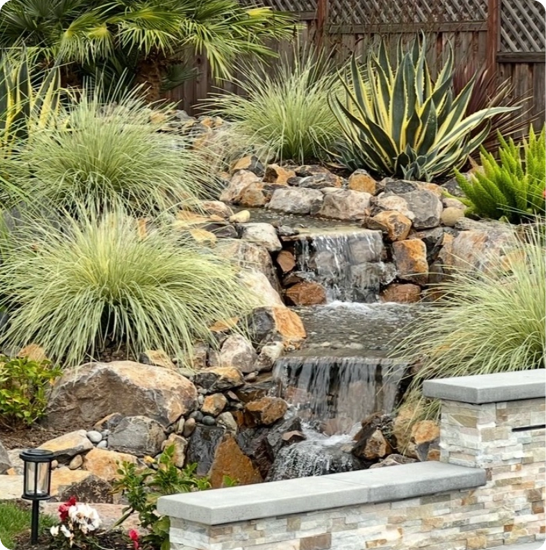 A serene backyard waterfall surrounded by rocks and greenery.