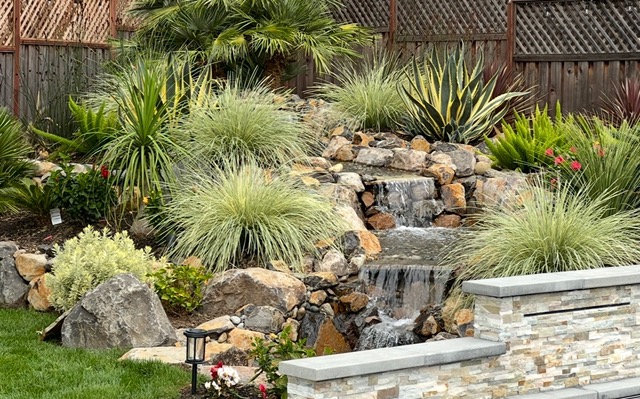 A serene garden waterfall surrounded by lush greenery and rocks.